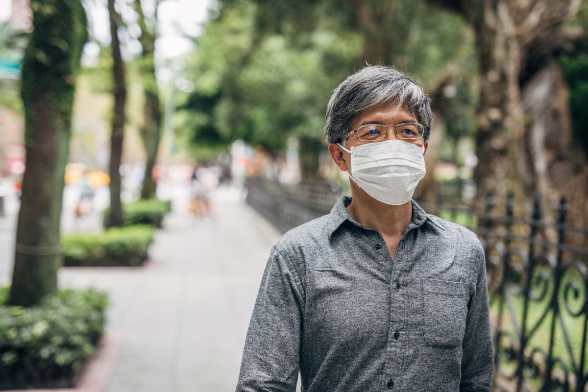 home asiàtic de més edat que camina amb màscara exterior
