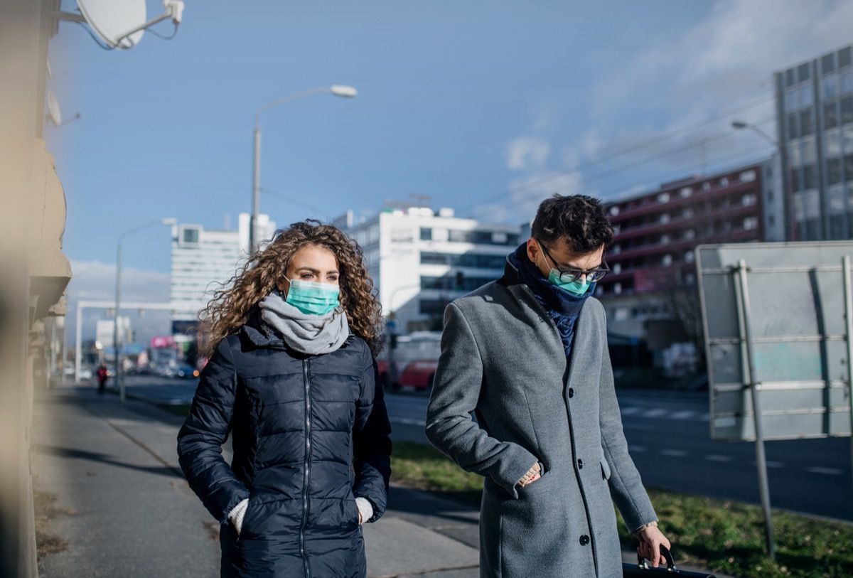balta sieviete un vīrietis staigā sejas maskās pilsētā
