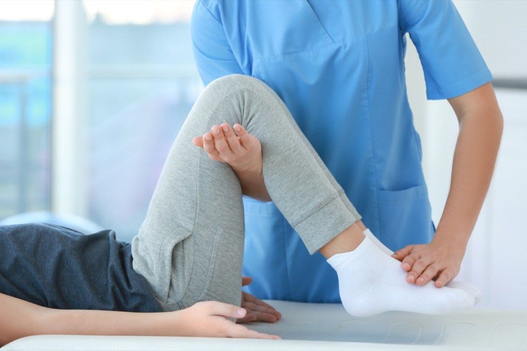 Ženska, ki si med fizikalno terapijo iztegne noge, nehajte lagati zdravniku