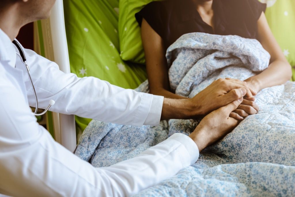 medicul ținând mâinile unui pacient pe un pat de spital