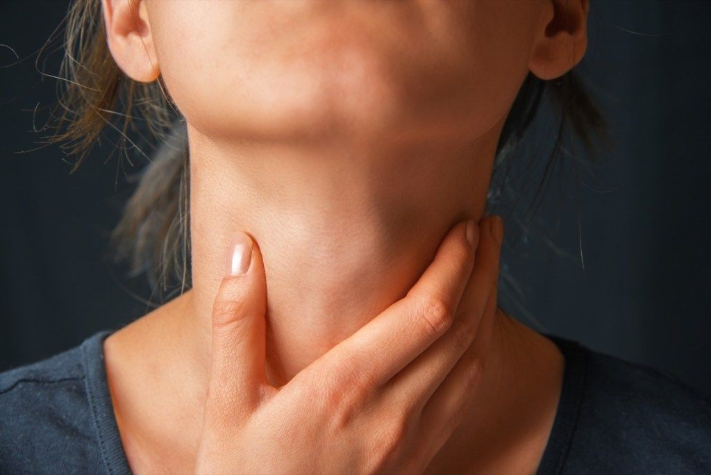 Žena se bolestivě dotýká krku (příznaky srdečního onemocnění)