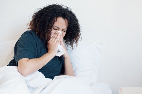 Kvinna som är sjuk och hostar i sängen