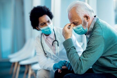 старији човек држећи главу од болова након што је од лекара у болници добио лоше вести током пандемије ЦОВИД-19.