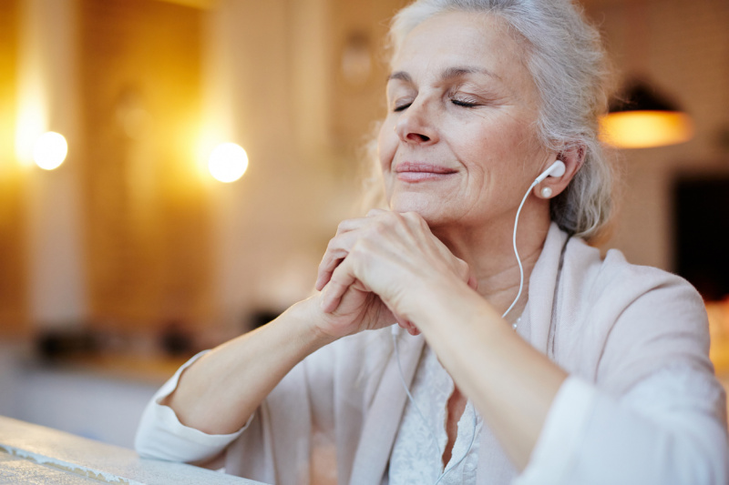   Uma mulher idosa sentada com os olhos fechados enquanto ouve fones de ouvido