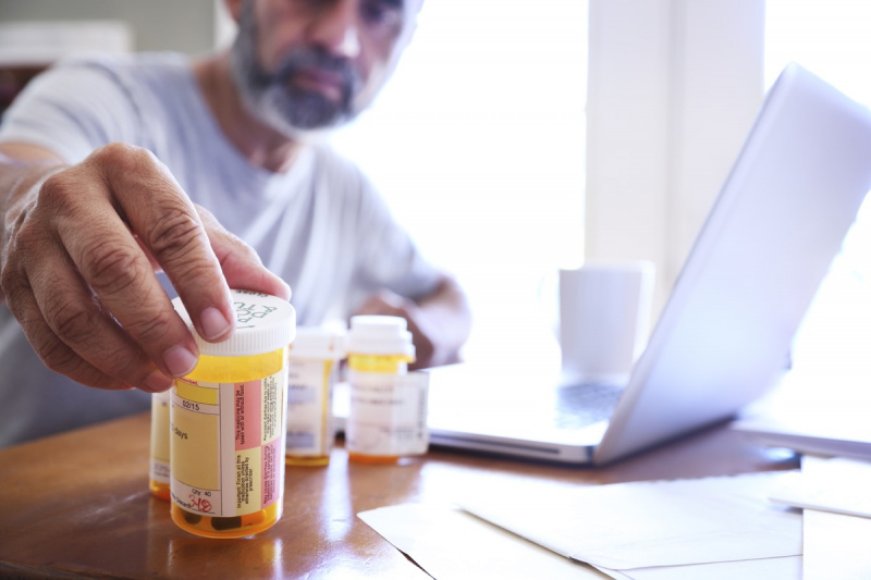   muškarac u kasnim pedesetima poseže za jednom od svojih bočica s lijekovima na recept dok sjedi za stolom u blagovaonici