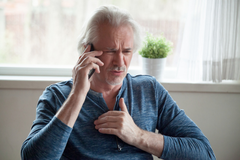   hombre blanco mayor con cabello largo agarrando el pecho y hablando por teléfono, luciendo preocupado
