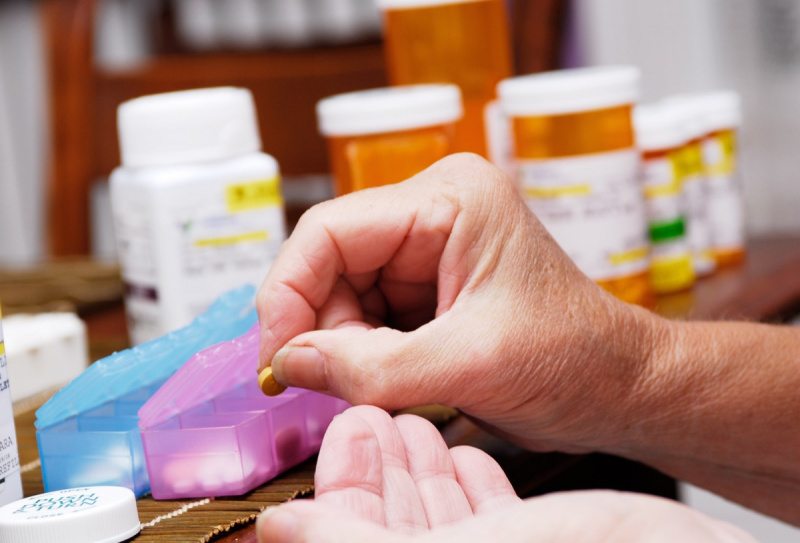   Възрастна жена взема лекарства от органайзера за хапчета