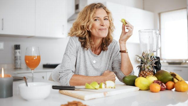   Foto de una mujer preparando y comiendo fruta antes de hacer un batido