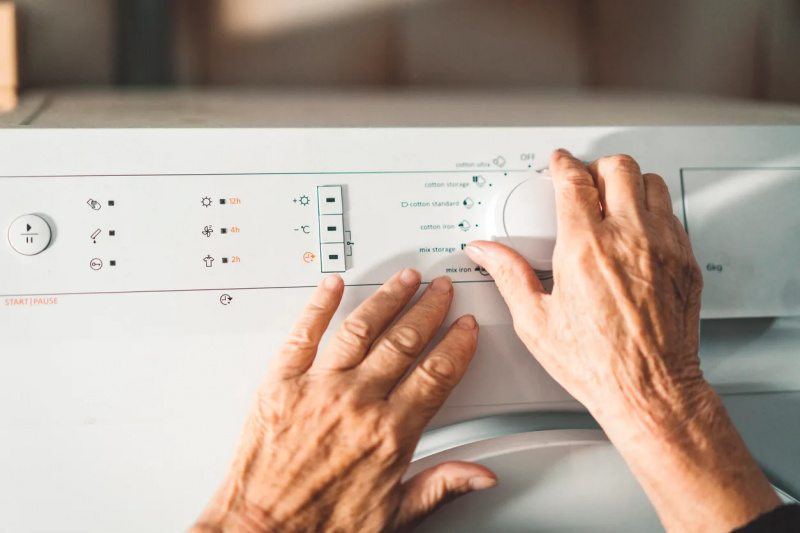   Tangan menyentuh kontrol mesin cuci atau pengering.