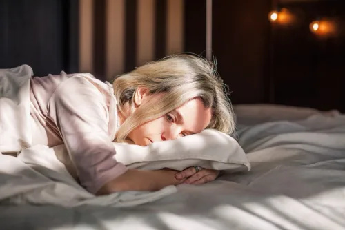   تھکی ہوئی درمیانی عمر کی عورت بستر پر لیٹی افسردگی محسوس کر رہی ہے۔