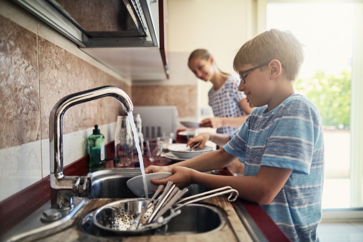 Kolme lasta pesee astioita keittiössä. Pojat ja tyttö auttavat yhdessä vanhempiaan.