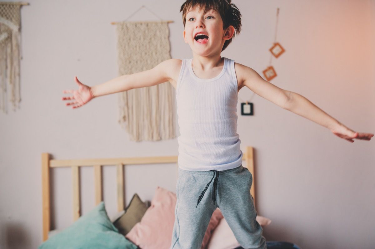 खुश शरारती लड़का सुबह में बिस्तर पर कूद रहा है। अति सक्रिय बच्चे, आकस्मिक जीवन शैली।
