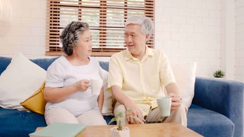 Pareja de ancianos hablando en el sofá mientras bebe café o té charla seria