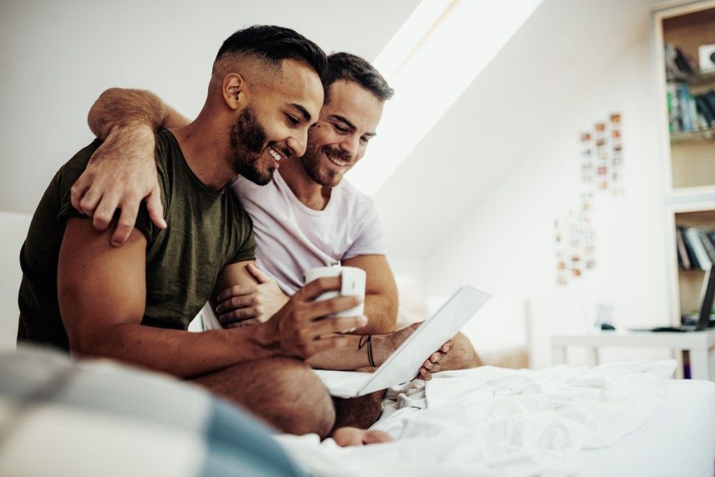Latino Mann und weißer Mann Homosexuell Paar betrachten einen Computer zusammen auf dem Bett