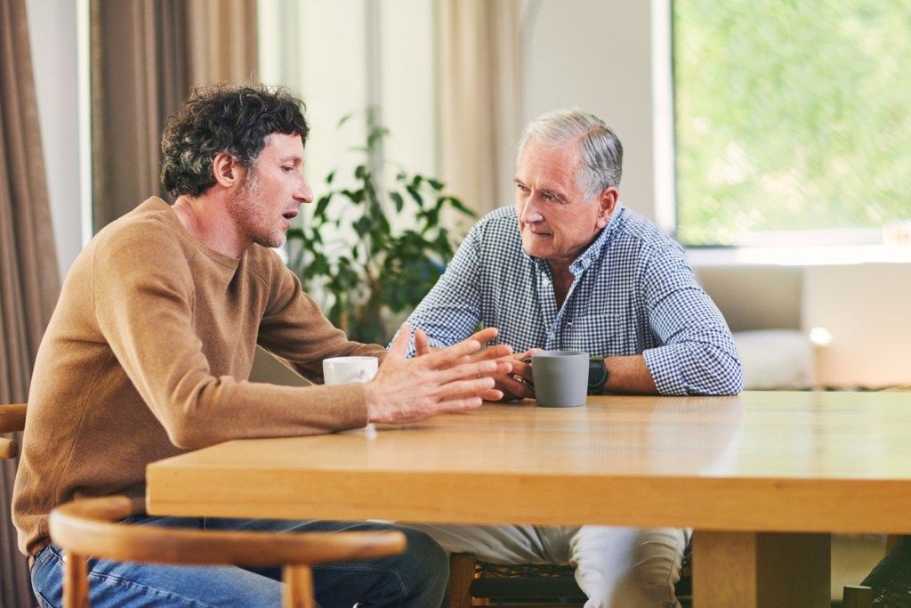 Ujęcie dojrzałego mężczyzny i jego ojca w podeszłym wieku, przy kawie i rozmowie w domu