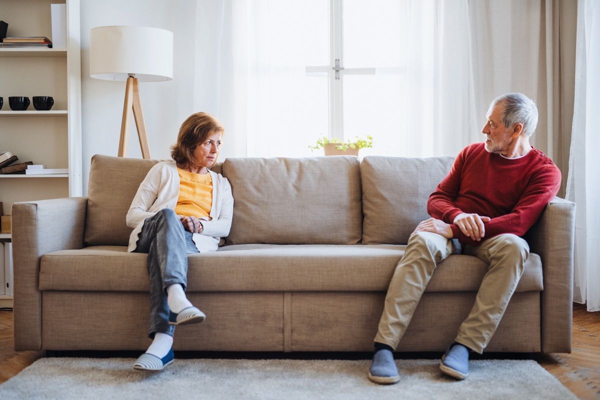 Una pareja senior enojada sentada en un sofá en casa, teniendo una discusión.