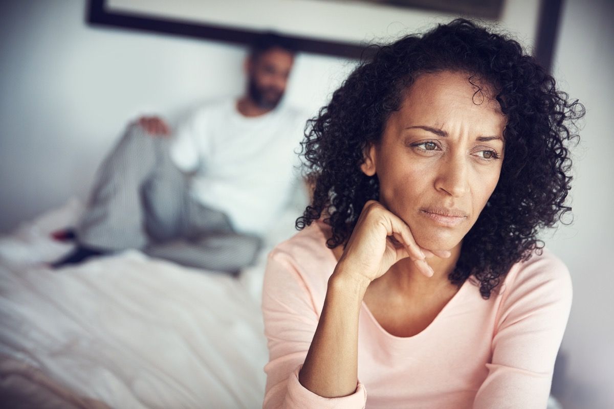 nainen näyttää järkyttyneeltä, kun aviomies makaa sängyssä hänen takanaan