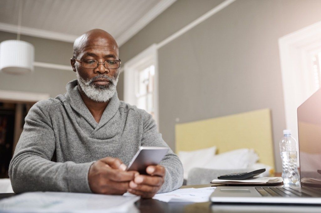 ældre sort mand kontrollerer sin telefon ved sit skrivebord