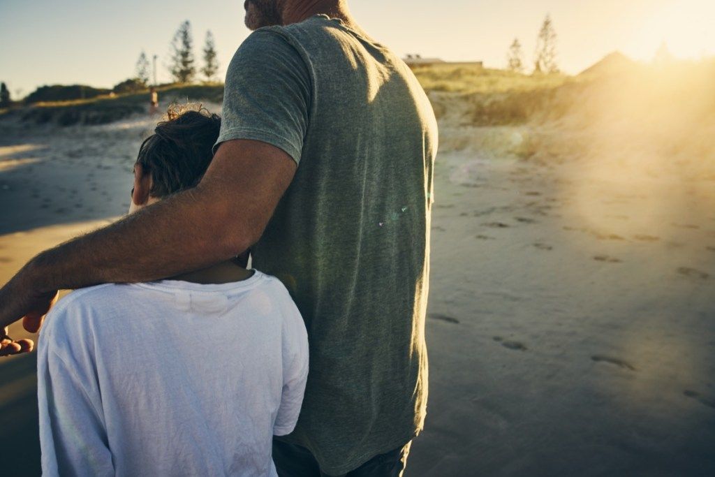 far og barn som går på stranden arm og arm