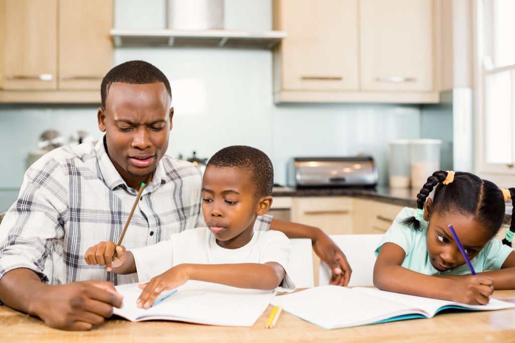 Tėtis ir vaikai, atliekantys namų darbus