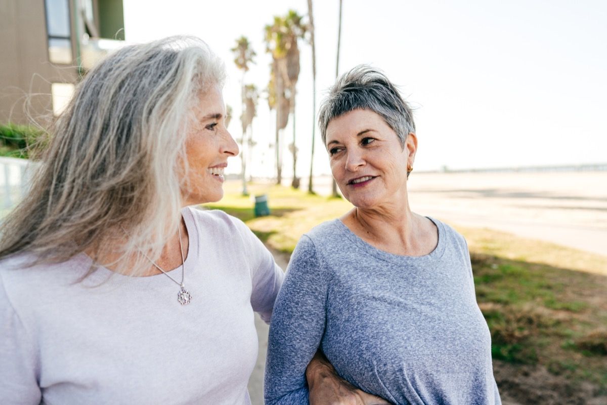 двойка по-възрастни бели жени се разхождат и се усмихват навън