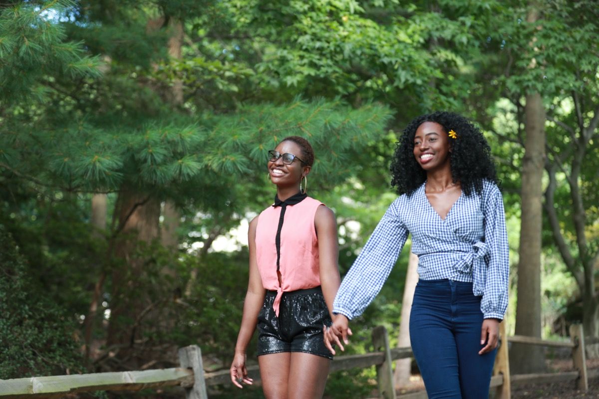 Zwei junge schwarze Frauen, die Hände halten und im Park gehen