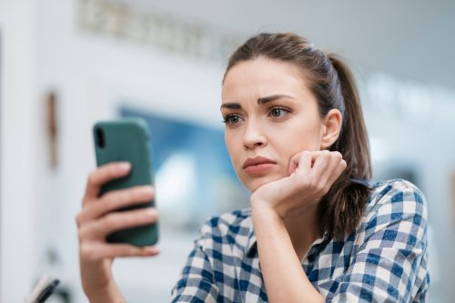   Млада жена гледа съобщение на телефона си със загрижено изражение на лицето.