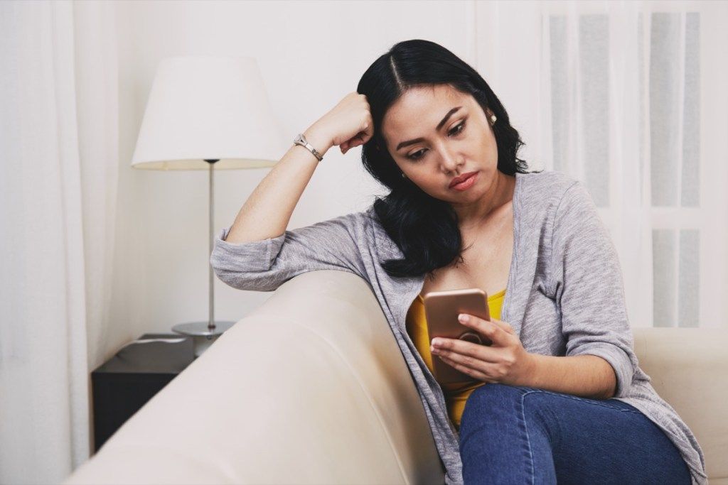 liūdna susimąsčiusi jauna filipinietė moteris, išmaniajame telefone skaitanti tekstinius pranešimus ar naujienas
