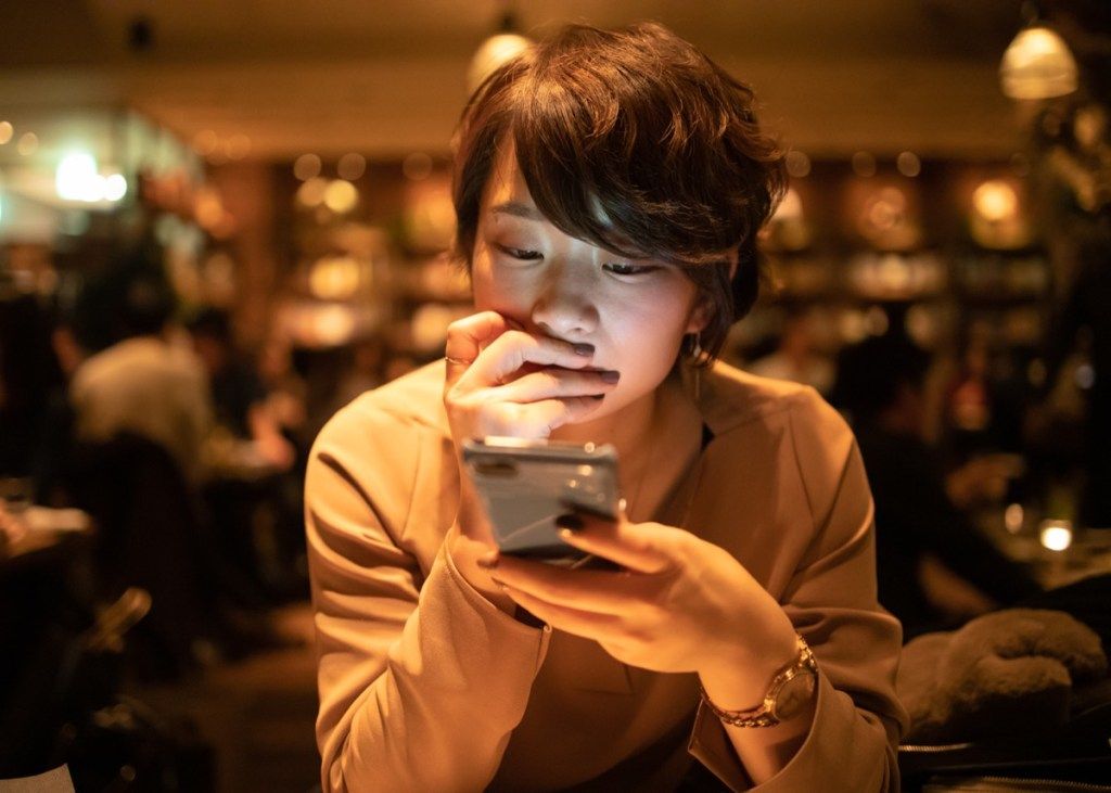 nuori nainen käyttää älypuhelinta kahvilassa työn jälkeen