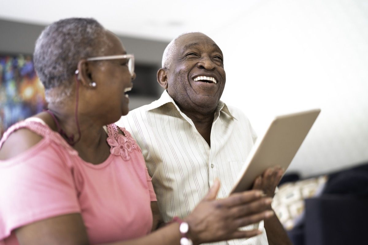 Vyresnė juoda pora juokiasi žiūrėdama į planšetinį kompiuterį