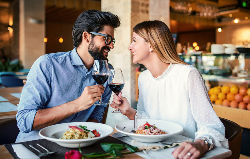   Romantisks pāris, kas bauda pusdienas restorānā, ēd pastu un dzer sarkanvīnu. Dzīvesveids, mīlestība, attiecības, ēdiena koncepcija
