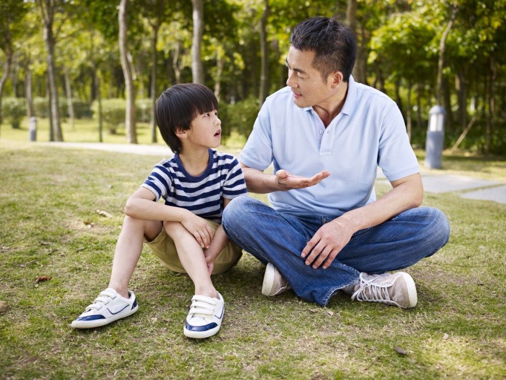 אב ובנו יושבים על מדשאה בפארק ומדברים, מכינים ילדים לגירושין