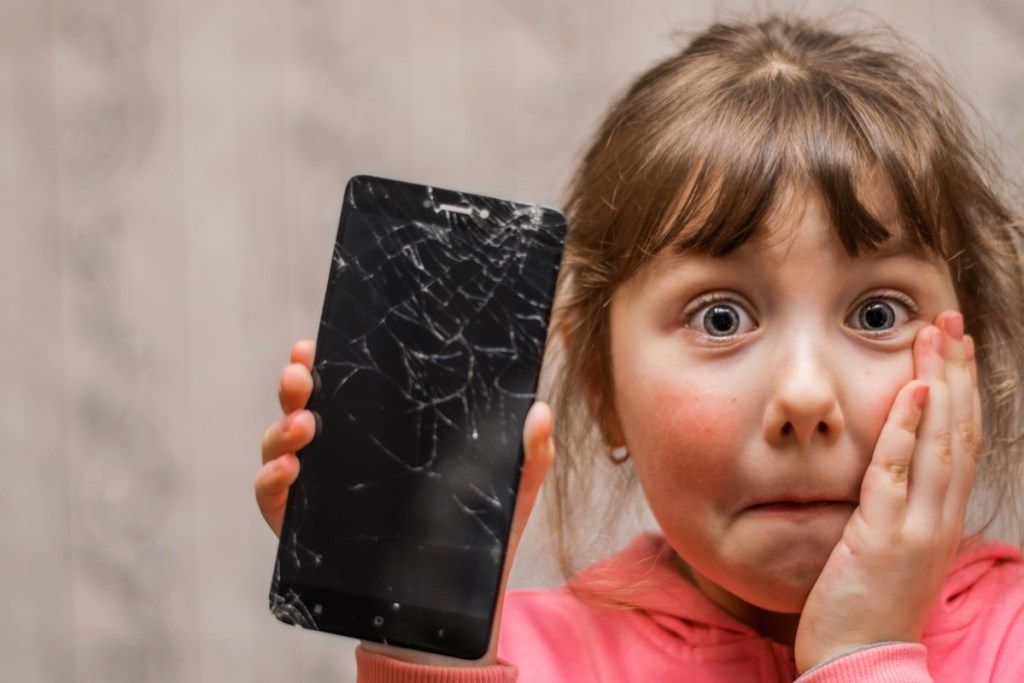 малко бяло момиче, държащо счупен телефон