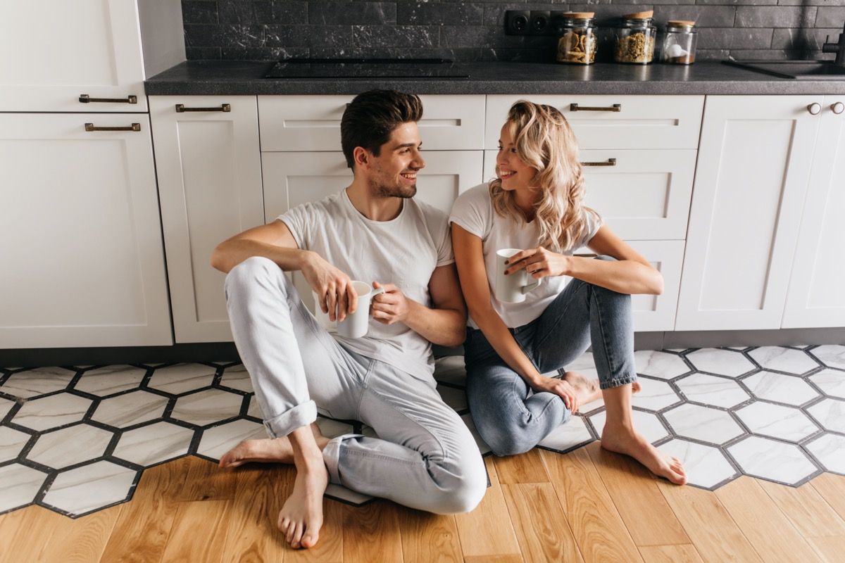 Nuori valkoinen mies ja nainen juo kahvia keittiön lattialla