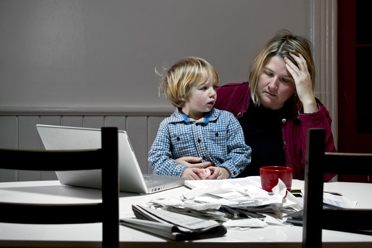 Donna depressa con figlio in grembo a tavola, sopraffatta da problemi finanziari, debiti, bancarotta.