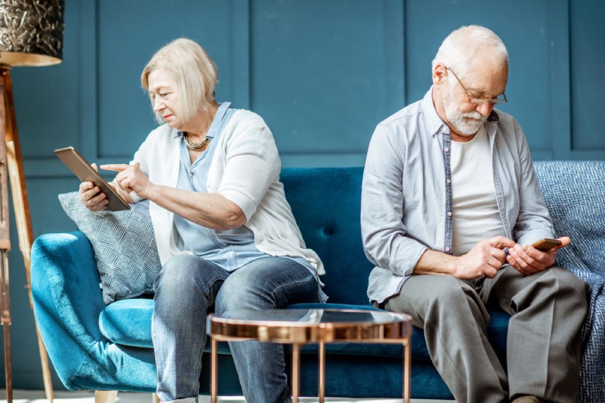 पुराने जोड़े स्मार्टफोन और टैबलेट, शिष्टाचार गलतियों का उपयोग करते हुए सोफे पर एक दूसरे की अनदेखी करते हैं