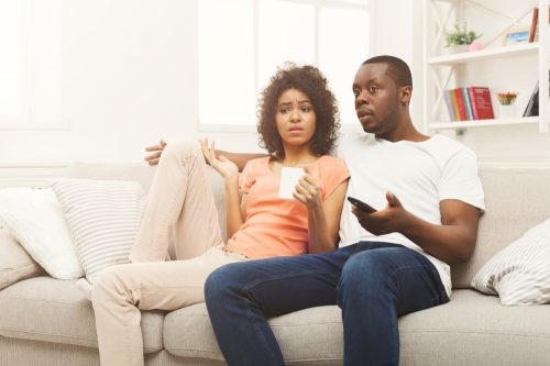   Млада двойка гледа телевизия с объркано или разочаровано изражение на лицата си