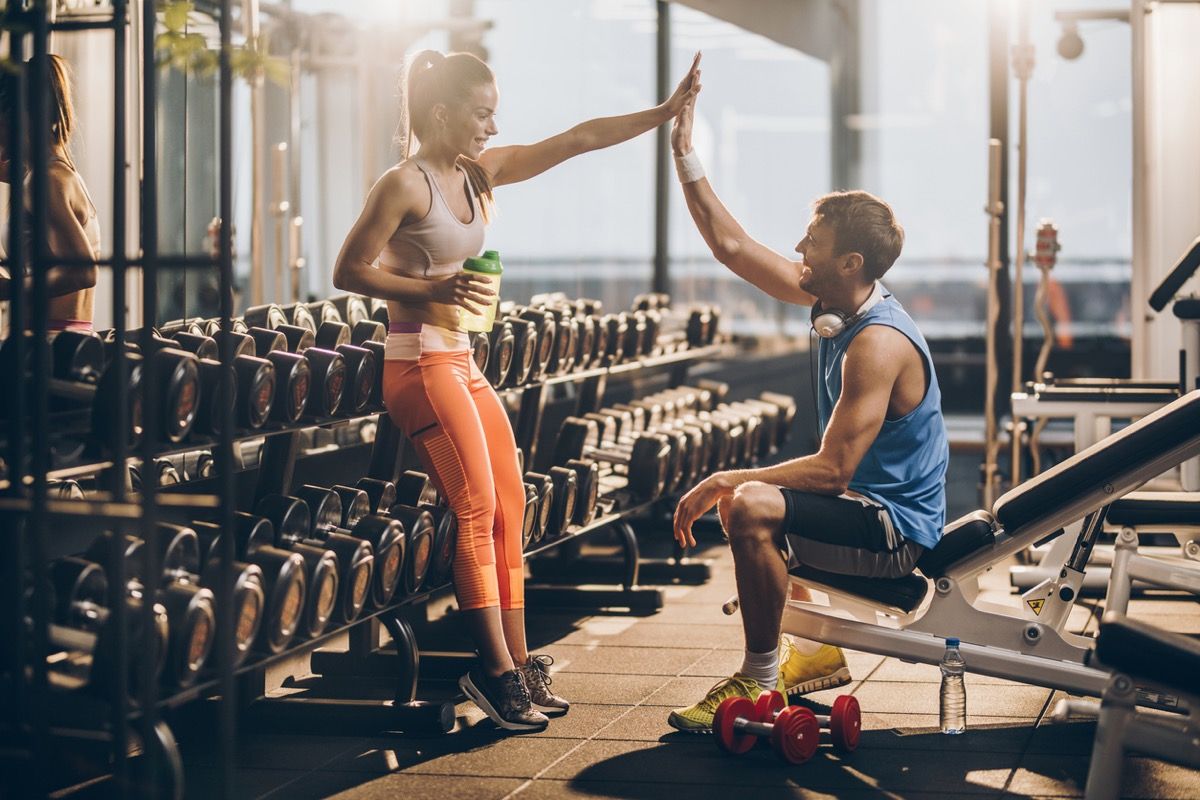 mujer blanca y hombre blanco dándose un máximo de cinco por las pesas en el gimnasio