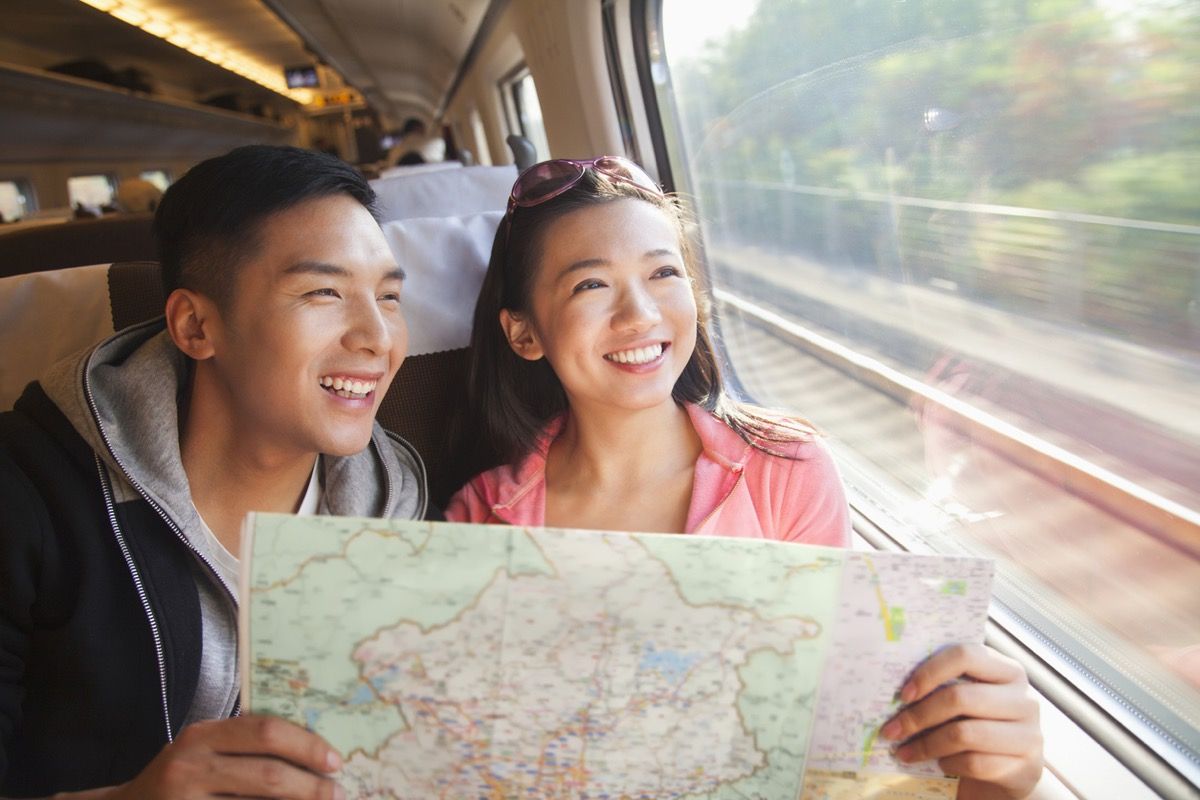 joven asiático y joven mujer asiática sosteniendo un mapa y mirando por la ventana en un tren