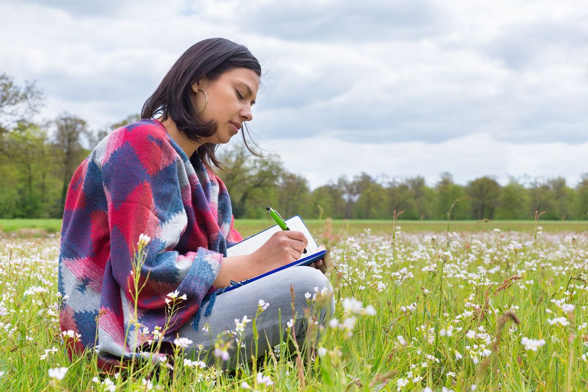 Mujer latina escribiendo en un diario en un prado
