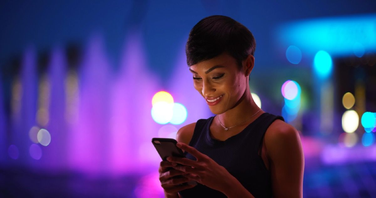 Joven mujer negra enviando mensajes de texto y sonriendo afuera por la noche