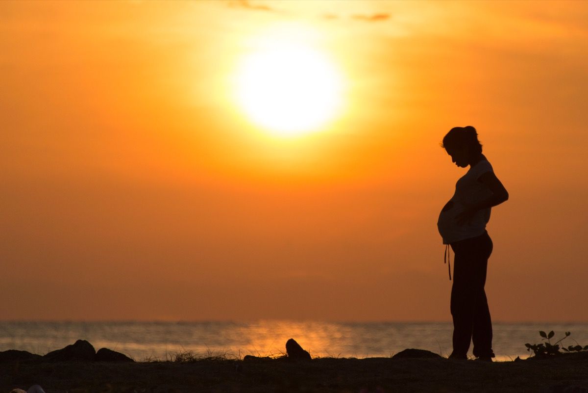 Remaja hamil berdiri di pantai dengan matahari terbenam di belakangnya, apa itu