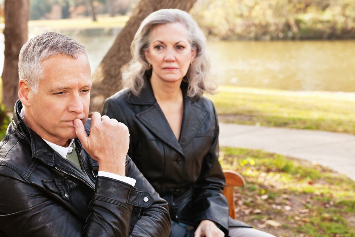 по-възрастна бяла двойка, изглеждаща нещастна на пейка в парка