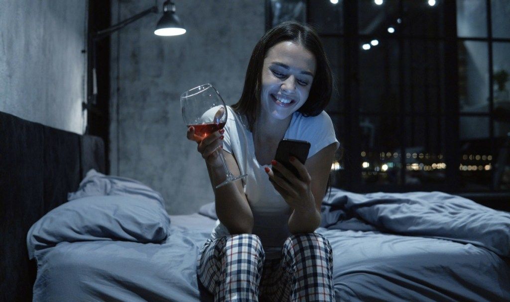 Žena chatuje po telefóne s pohárom vína