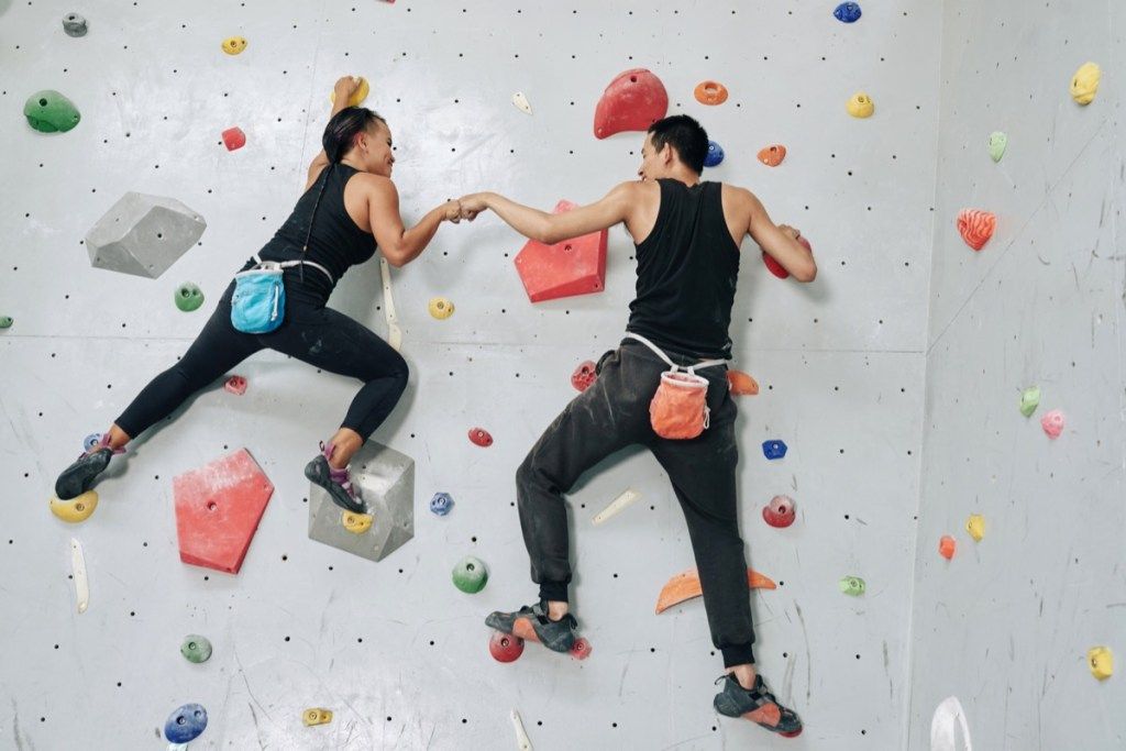 Vedeți în spate bărbatul și femeia care se antrenează în echipă și se lovesc de mâini în timp ce atârnați pe un perete de alpinism