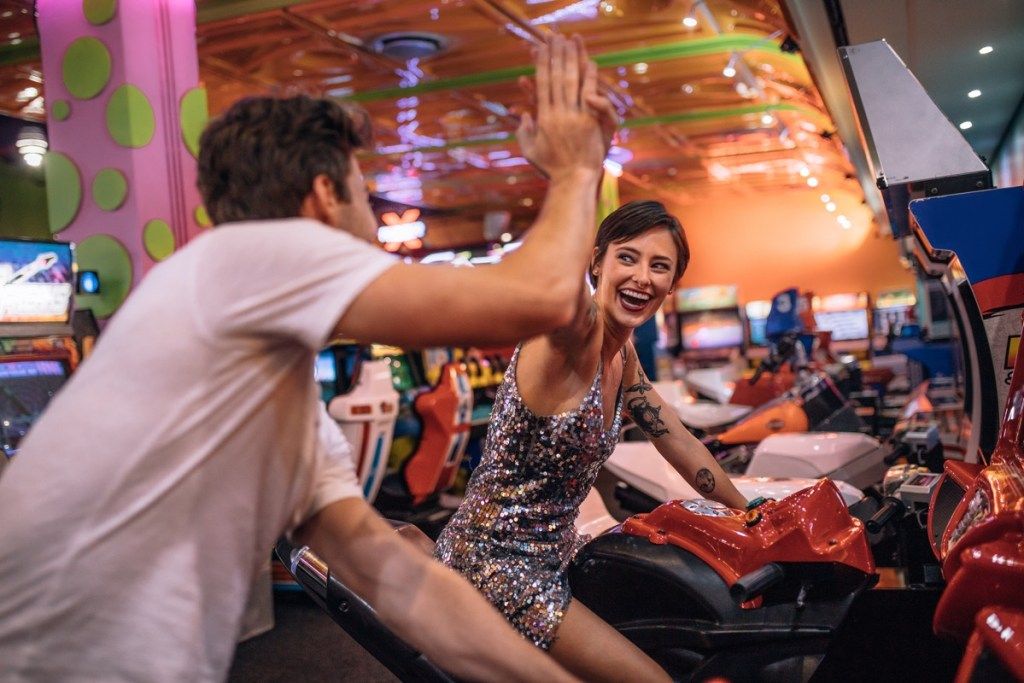 Pasangan saling memberi nilai tinggi ketika bermain permainan lumba basikal di arcade permainan. Pasangan menikmati permainan lumba arked di ruang permainan