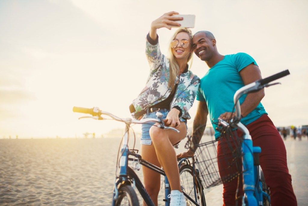 casal interracial atraente em bicicletas tomando selfie com sinais de você