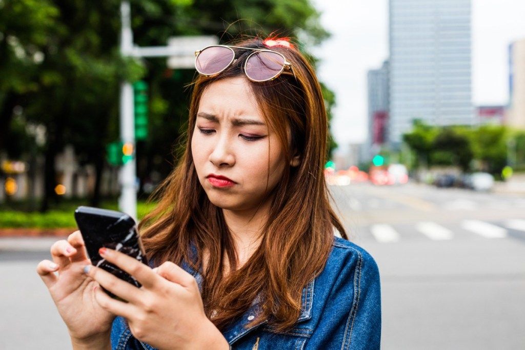 หญิงสาวชาวเอเชียหน้าตาผิดหวังขณะใช้โทรศัพท์บนถนน