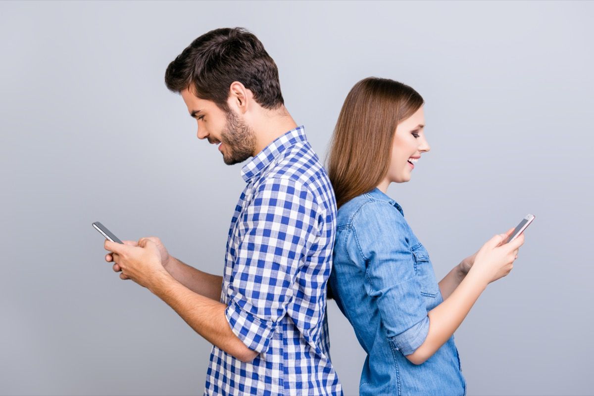 Mann og kvinne, stående, rygg mot rygg, texting