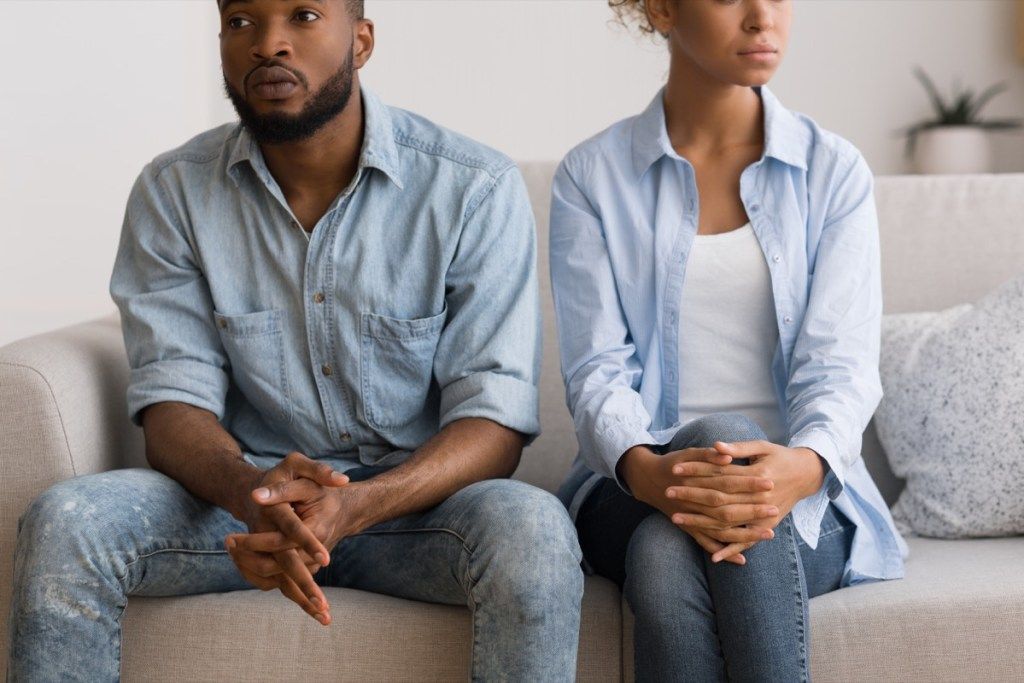 ung sort kvinde og mand sidder i sofaen ser ked af det